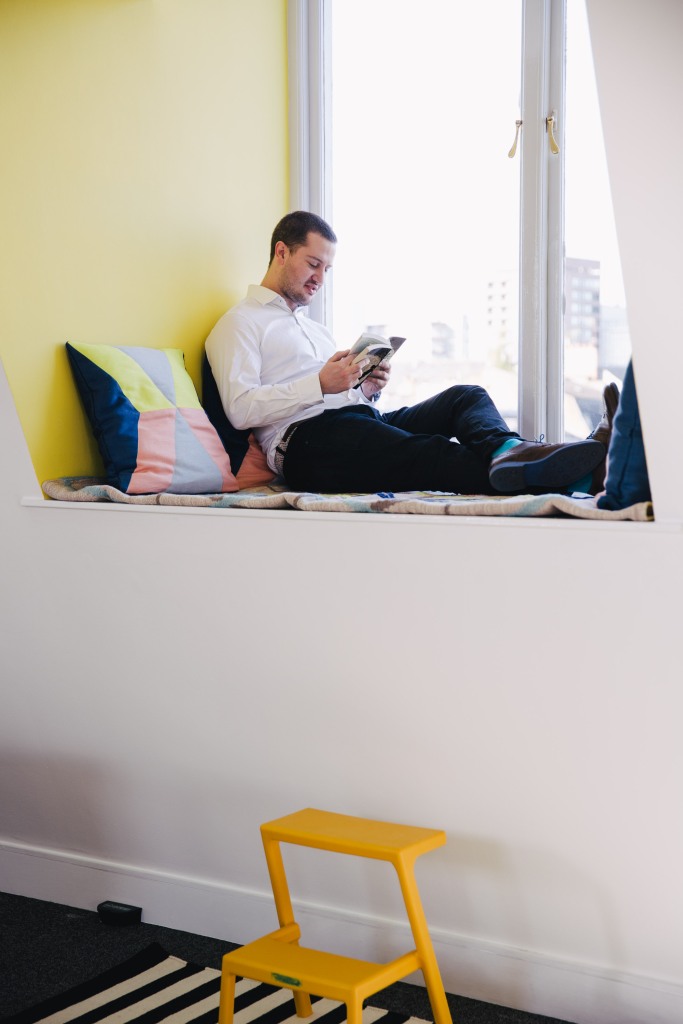 Gentleman relaxing with novel on window sill in Soho Labs office